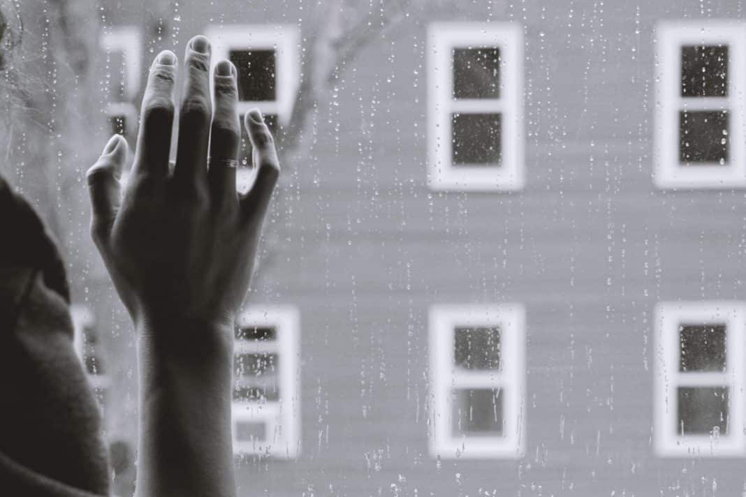 A lonely hand on a window pain while it rains outside