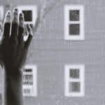 A lonely hand on a window pain while it rains outside