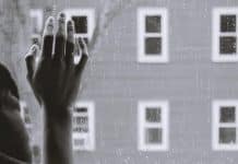 A lonely hand on a window pain while it rains outside