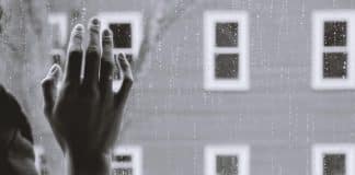 A lonely hand on a window pain while it rains outside