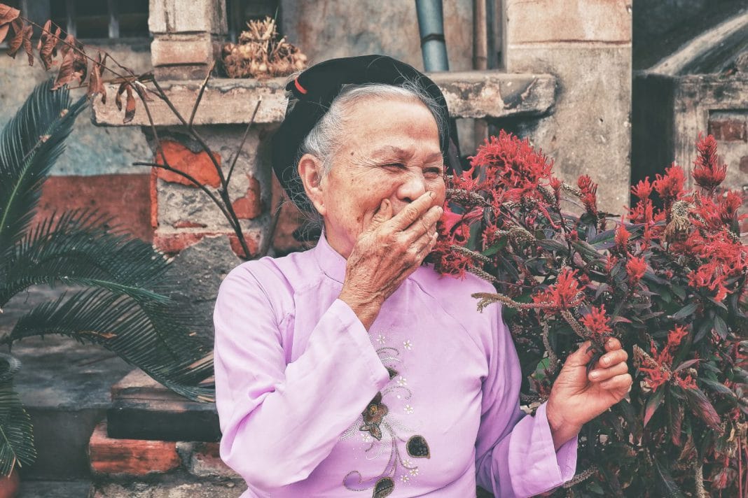 An elderly woman laughs and covers her mouth with her hand