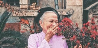 An elderly woman laughs and covers her mouth with her hand