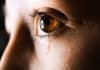 A close up of a person's eye, with a tear rolling down their cheek