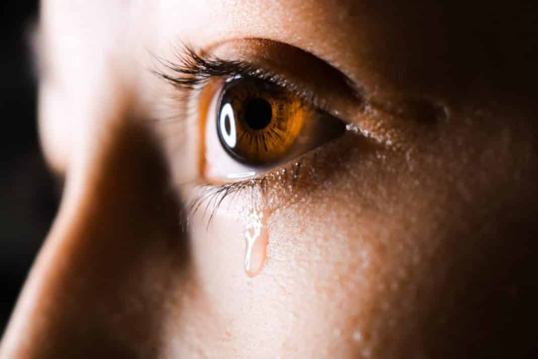 A close up of a person's eye, with a tear rolling down their cheek