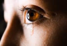 A close up of a person's eye, with a tear rolling down their cheek