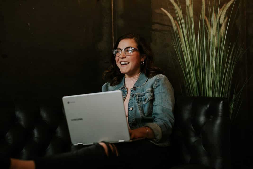 A brown-haired girl with glasses smiles and uses a computer