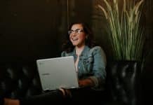 A brown-haired girl with glasses smiles and uses a computer