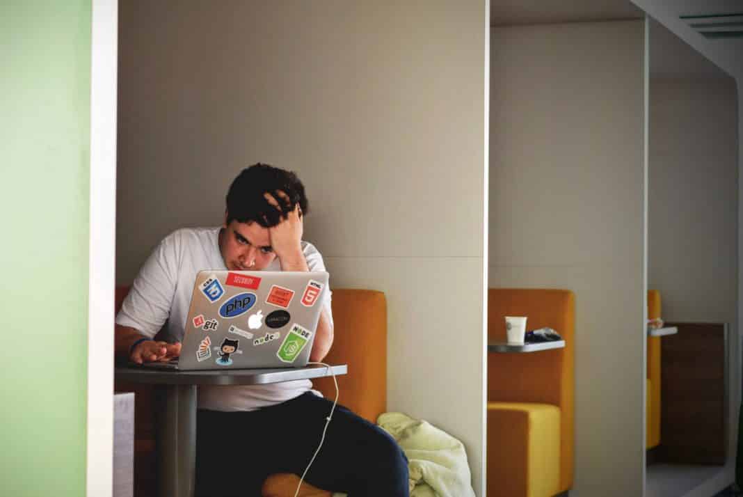 A stressed student uses his laptop at a desk