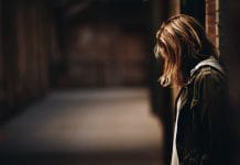A young woman looks down in a dark alleyway