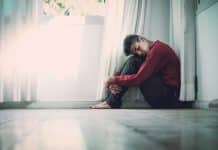 A man sits on a bathroom floor with his knees pulled up to his chest