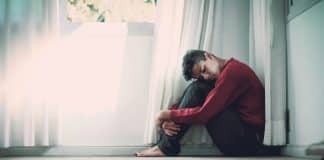 A man sits on a bathroom floor with his knees pulled up to his chest