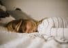A girl lays on a bed, her hair covering her face, looking exhausted