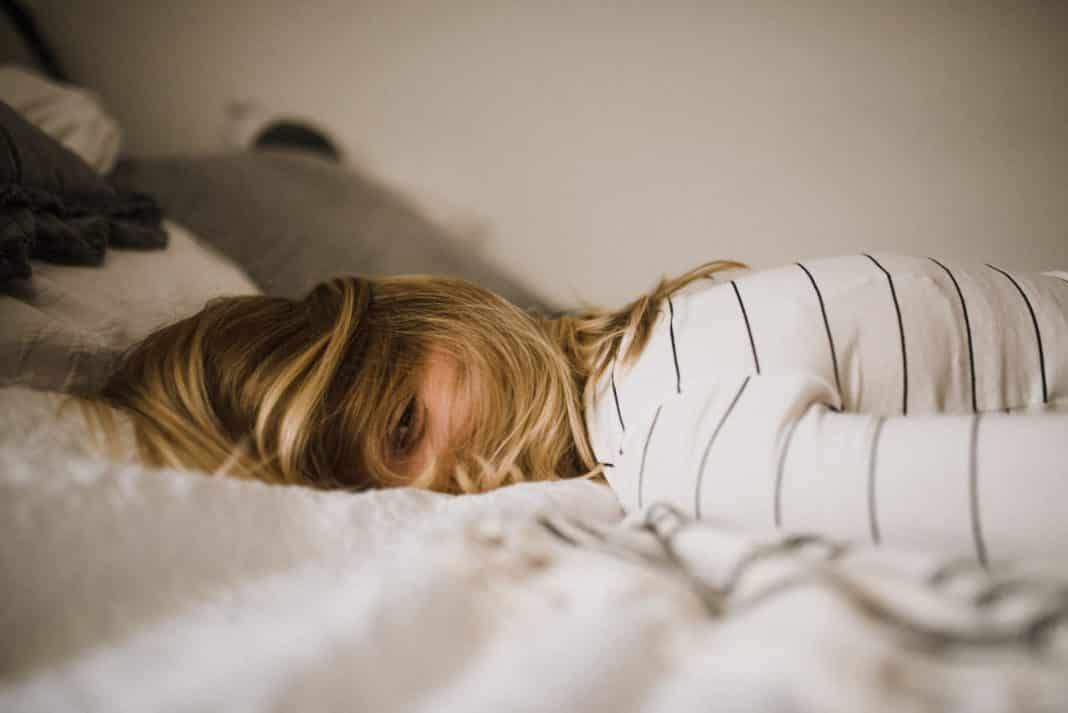 A girl lays on a bed, her hair covering her face, looking exhausted