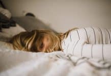 A girl lays on a bed, her hair covering her face, looking exhausted