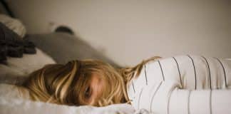 A girl lays on a bed, her hair covering her face, looking exhausted
