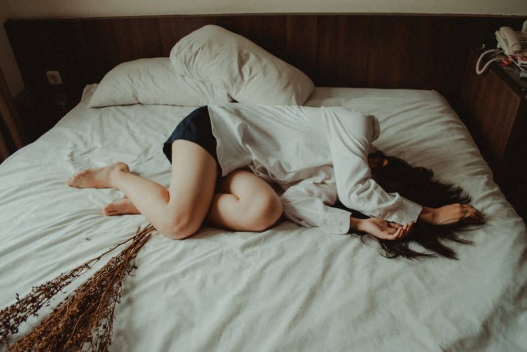 A young woman curls up on a bed, in distress