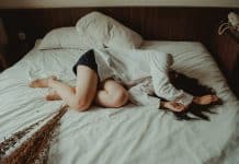 A young woman curls up on a bed, in distress