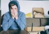 A young man in a hoodie covers his face with his hands
