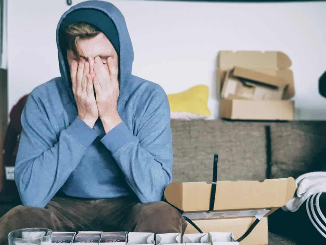 A young man in a hoodie covers his face with his hands