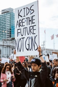 A young man holds up a sign saying 'Kids are the future, not guns'