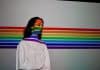 A woman stands in front of the LGBT flag.