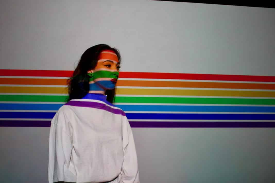 A woman stands in front of the LGBT flag.