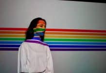 A woman stands in front of the LGBT flag.
