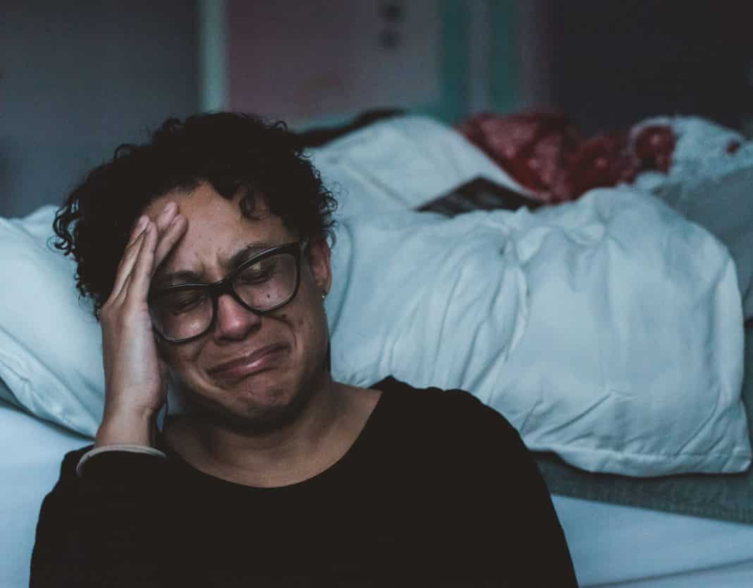A woman cries, sitting by her bed