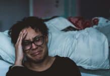 A woman cries, sitting by her bed