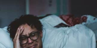A woman cries, sitting by her bed