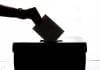 A hand puts a voting slip into a ballot box