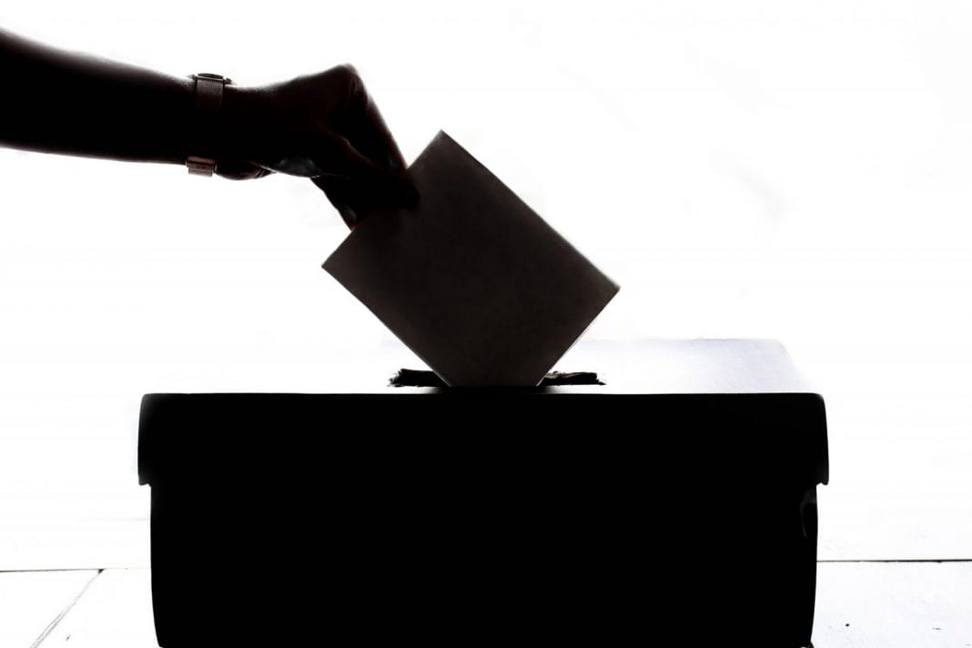 A hand puts a voting slip into a ballot box