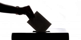 A hand puts a voting slip into a ballot box