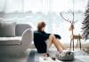A young woman looks sad, sitting on a floor surrounded by Christmas decorations