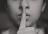 A black and white image of a woman with a finger over her lips