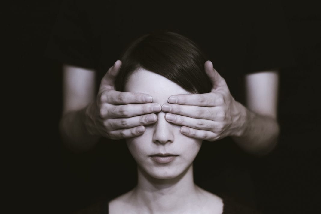 A young woman has her eyes covered by a pair of hands