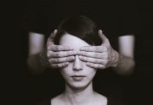 A young woman has her eyes covered by a pair of hands