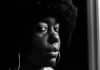 A young black woman with natural hair looks at the camera