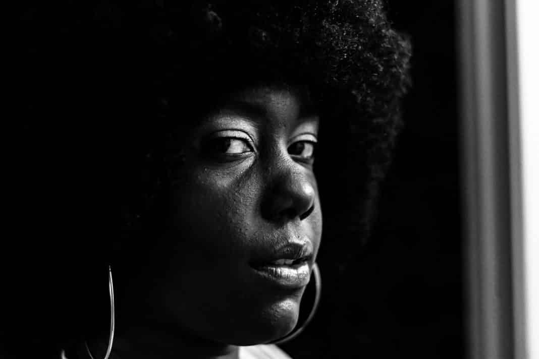 A young black woman with natural hair looks at the camera