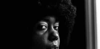 A young black woman with natural hair looks at the camera