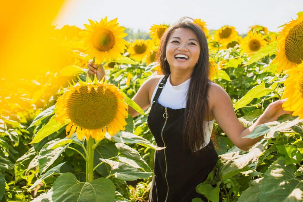A young Asian woman smiles, surrounded by giant sunflowers