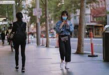 A young Chinese woman wears a mask while walking along a street texting