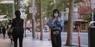 A young Chinese woman wears a mask while walking along a street texting