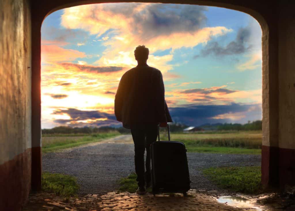 A young man with a suitcase looks at a vibrant sky