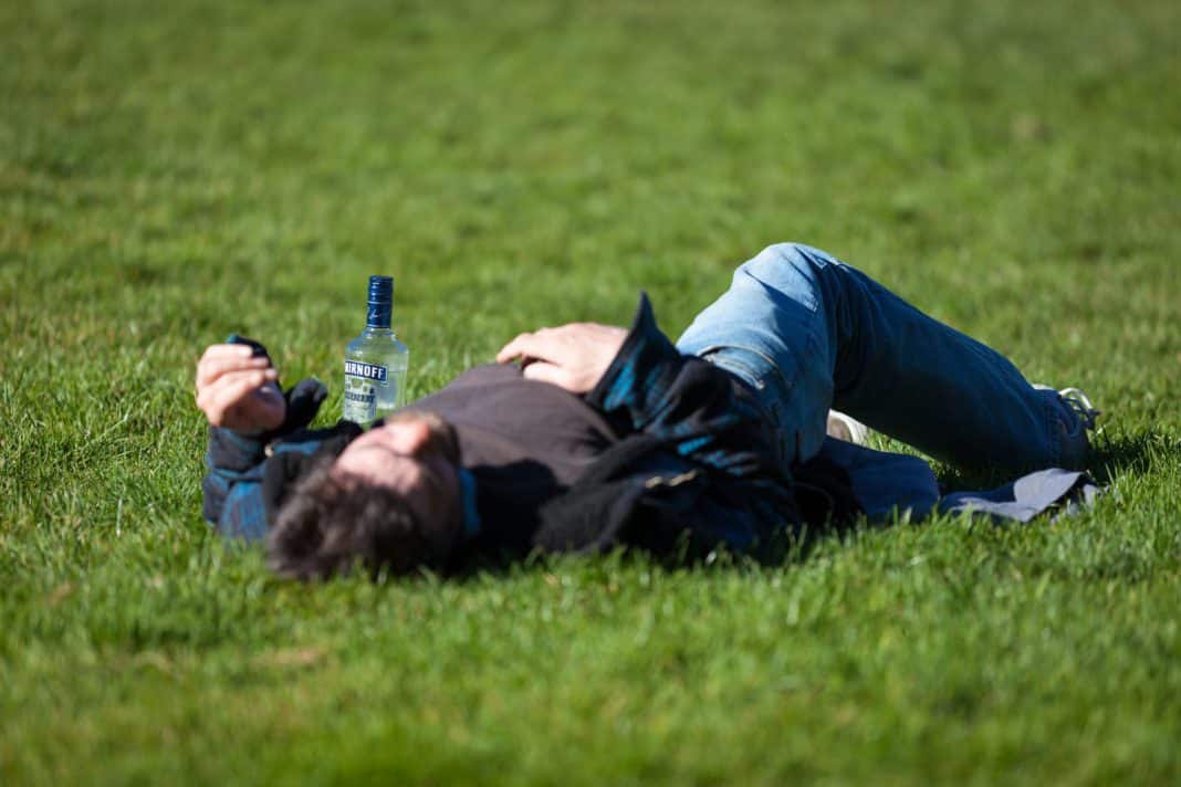 A young man passed out on grass, next to a bottle.