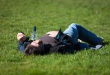 A young man passed out on grass, next to a bottle.