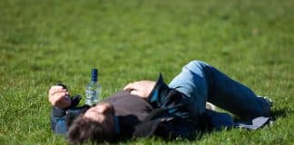 A young man passed out on grass, next to a bottle.