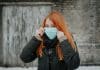 A red-haired woman wears a surgical mask over the lower half of her face