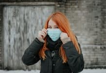 A red-haired woman wears a surgical mask over the lower half of her face