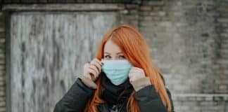 A red-haired woman wears a surgical mask over the lower half of her face